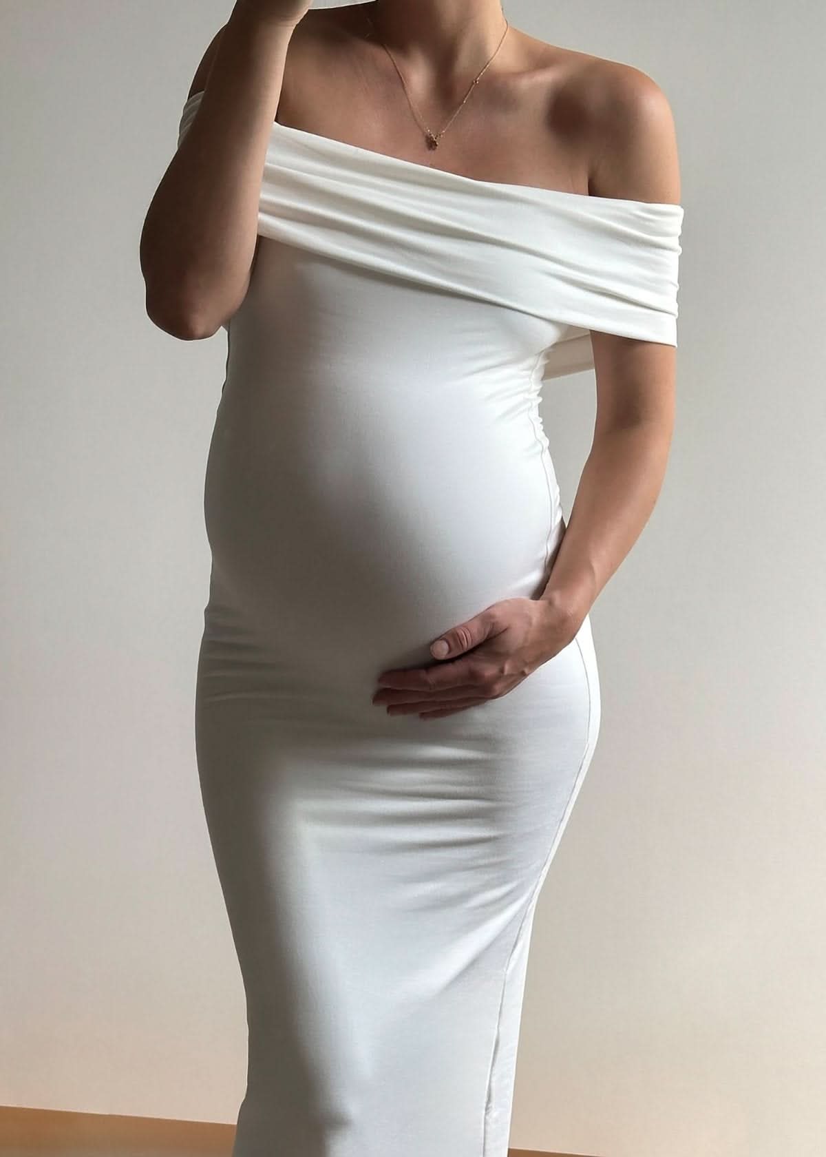 Person wearing a white off-shoulder dress against a plain background